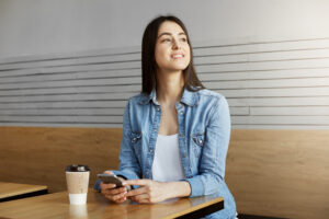 A Solidão Não se Cura com Pressa: O Valor de Esperar pelo Propósito 1 joyful attractive girl with dark hair sitting cafe drinks coffee chatting with friend smartphone then turning head see boyfriend through window 1