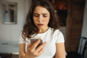 serious attractive young woman holding smart phone frowning reading sad news